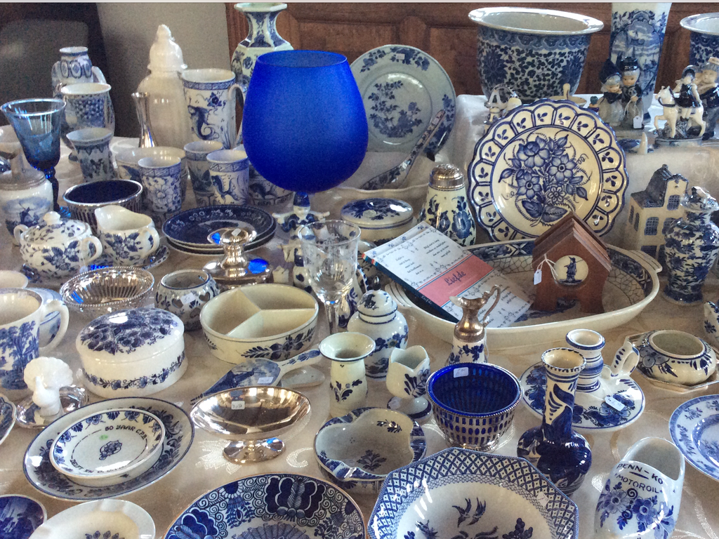 Delft blue earthenware with plates, vases, cups and a blue glass on a lace cloth