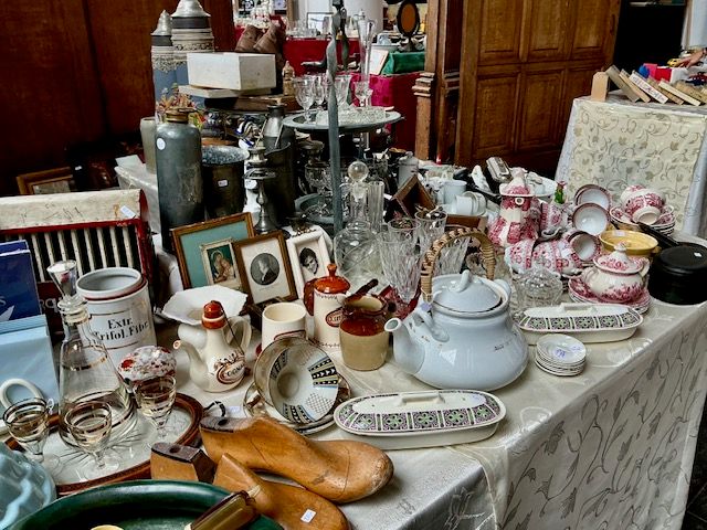 Marktkraam met rood-wit servies, houten klompmallen, kannen, lijstjes en een theepot op een kleed