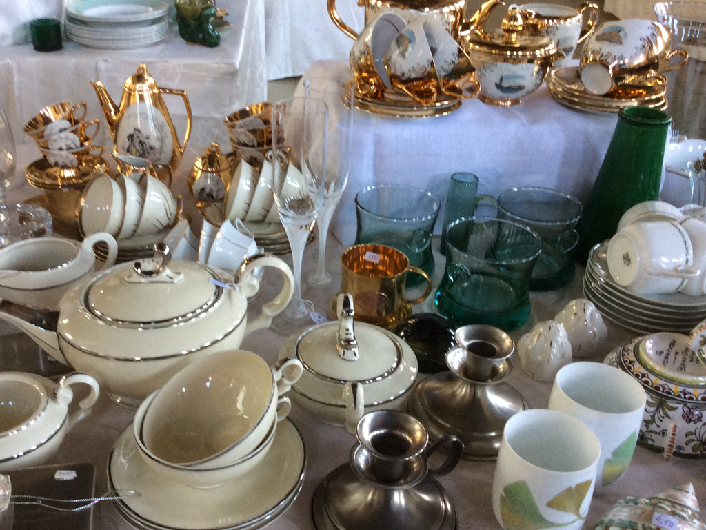 Wit servies met zilverrand en goudkleurig theeservies naast groene glazen en tinnen kandelaars