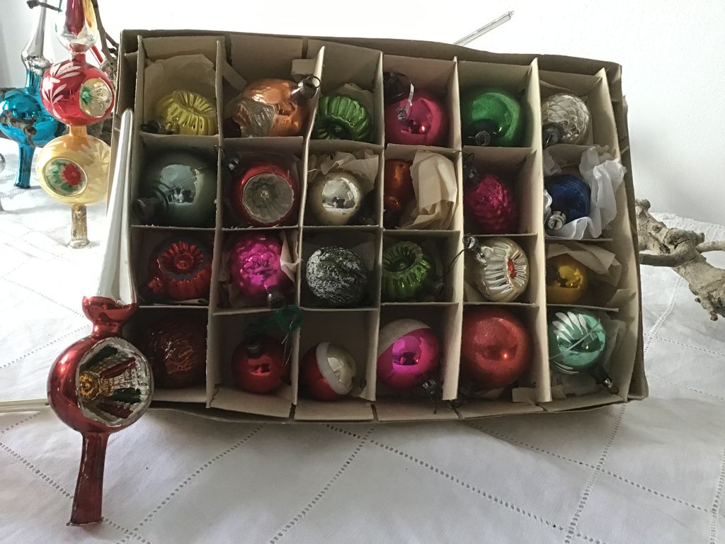 Doos met vakjes vol kleine antieke kerstballen, ervoor een rode glazen piek