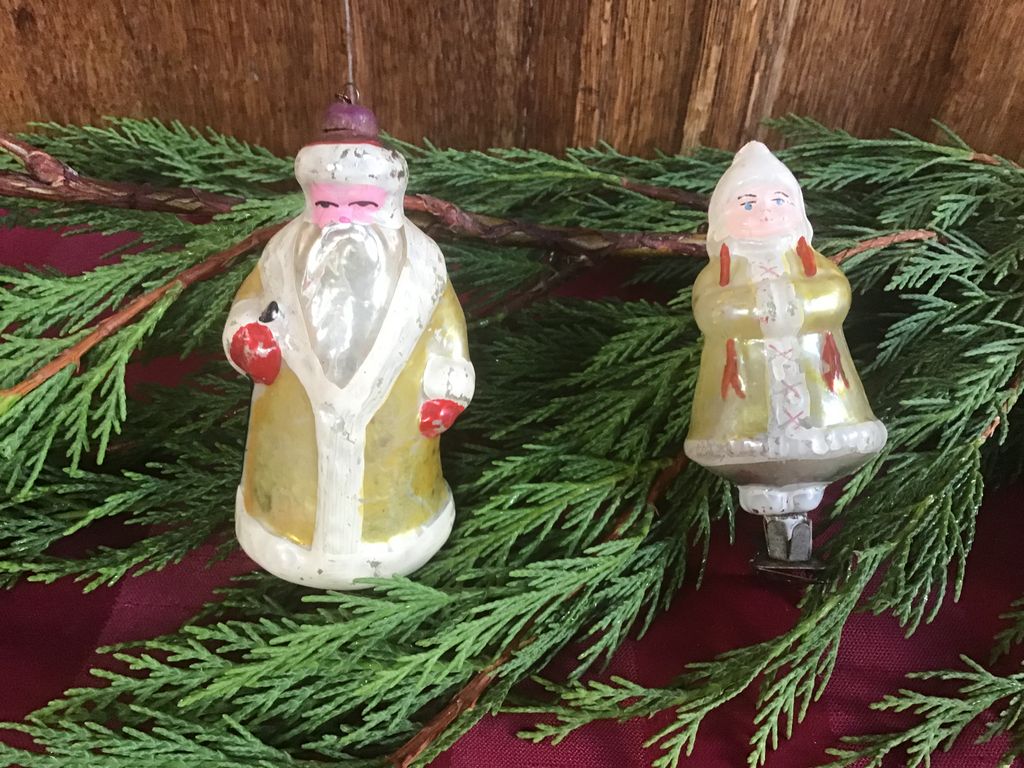 Twee antieke glazen figuurtjes in lange gele jassen, een met baard