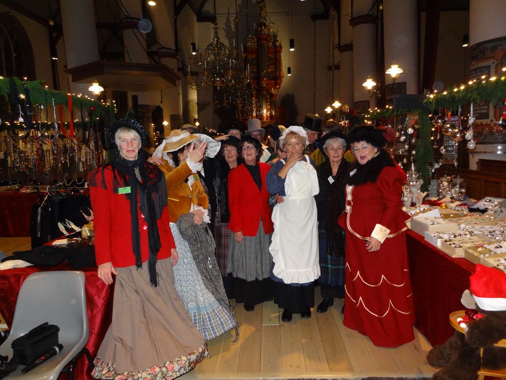 Groep vrijwilligers in Dickens-kleding poseert tussen de kramen