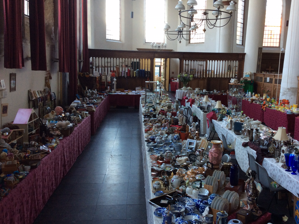 View of the church hall with market stalls full of crockery, glass and curiosities on tables with red and white cloths