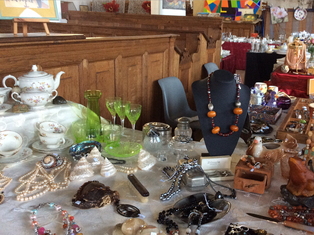 Bead and pearl necklaces, green wine glasses and floral crockery on a white cloth in the church