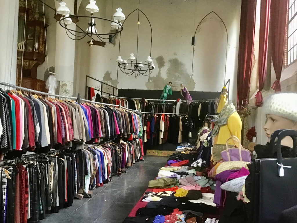 Lange rekken met kleding en tafels met tassen en hoeden in de kerk, onder kroonluchters