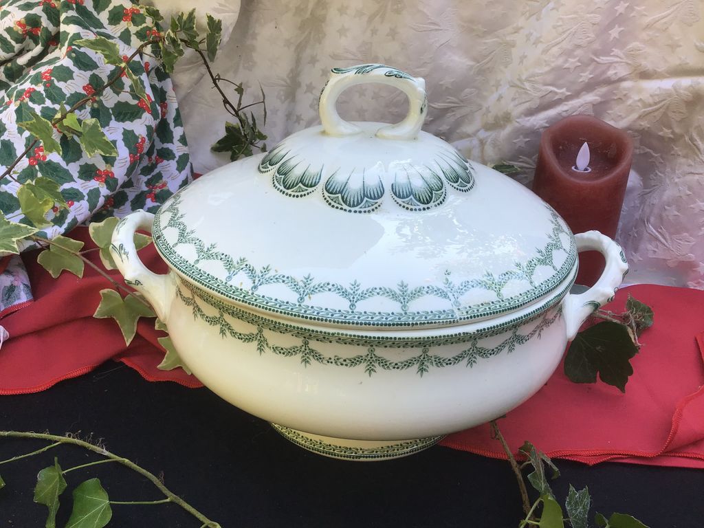 White soup tureen with a green rim pattern on a red cloth with ivy