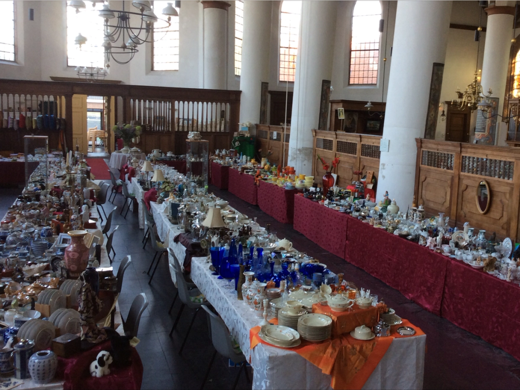 Long market stalls full of crockery, glassware and crystal with red and orange cloths in the church