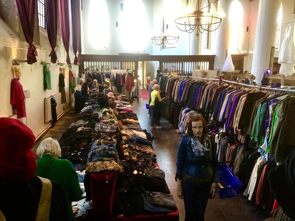 Bezoekers lopen langs kledingrekken en tafels in de kerk