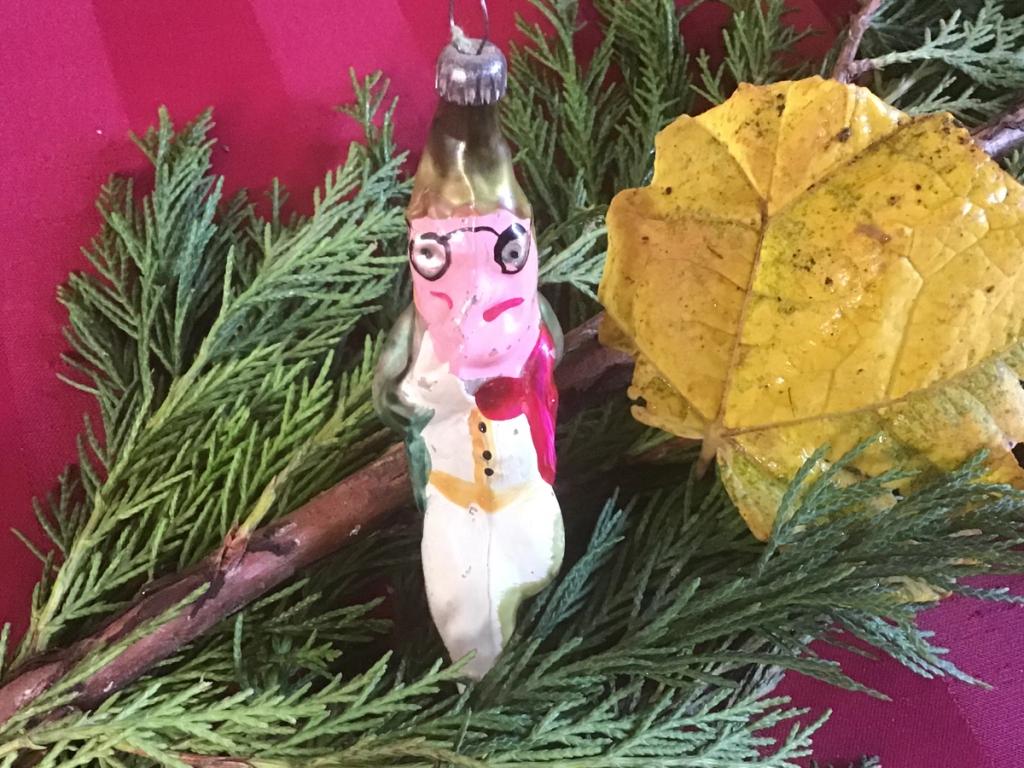 Glazen kerstversiering in de vorm van een man met bril, naast een geel blad
