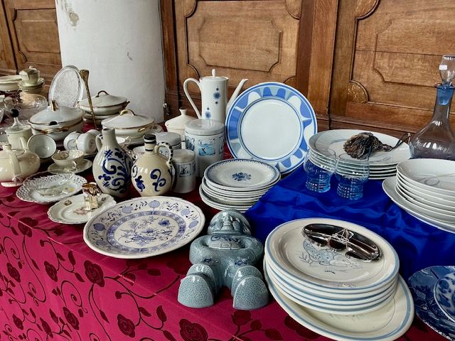 Blauw-wit en wit servies, borden, terrines, kannen en een grijs beeldje op een tafel met rood kleed met rozen