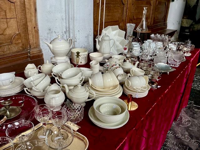 Roomkleurig servies met ribbelpatroon: theepotten, kopjes en kommen op een tafel met rood kleed in de kerk
