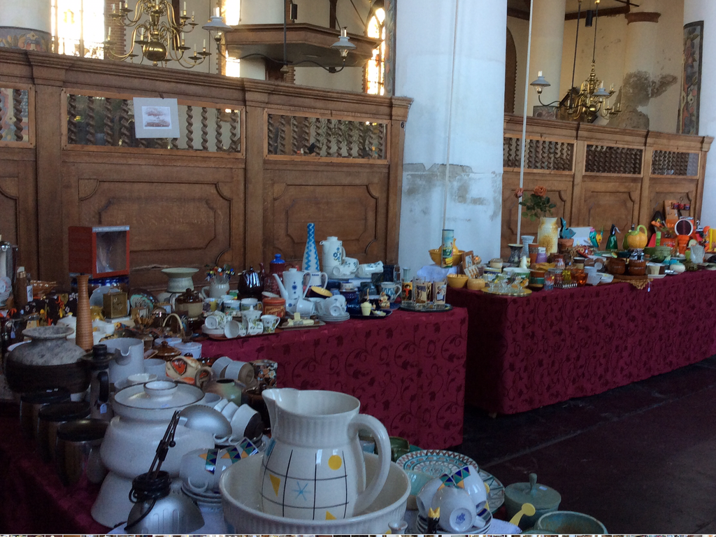 Market stalls with crockery, jugs and cups on tables with red cloths in the church