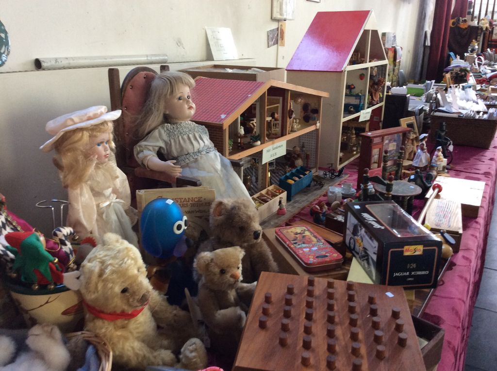 Dolls, old teddy bears and a doll's house on a table with a red cloth
