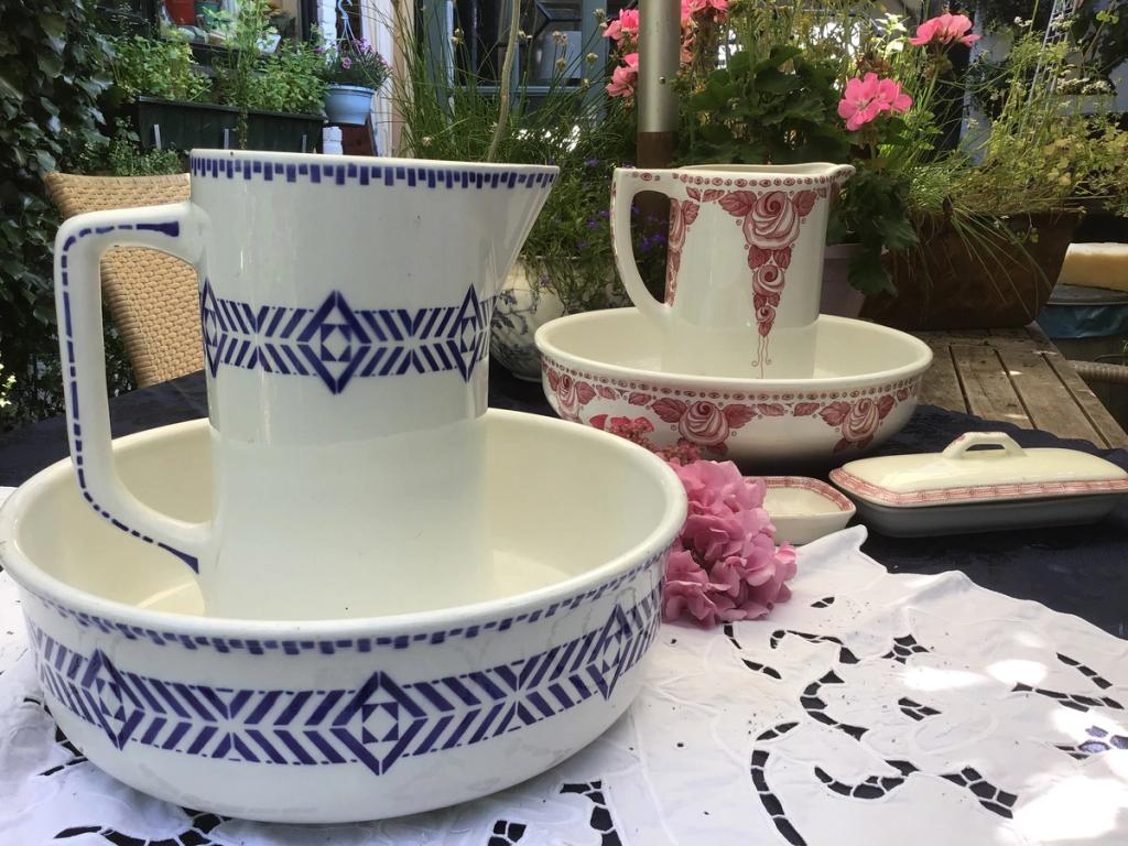 Witte kan en waskom met blauw patroon en een rode kan en kom op een kanten kleed