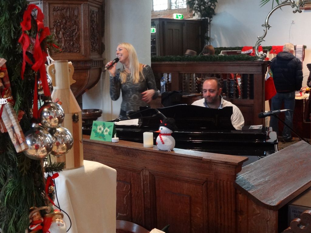 Zangeres en pianist spelen bij het orgel, naast kerstballen en een sneeuwpop