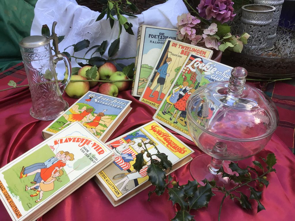 Old children's books, a glass beer mug and a glass sweet dish on a red cloth