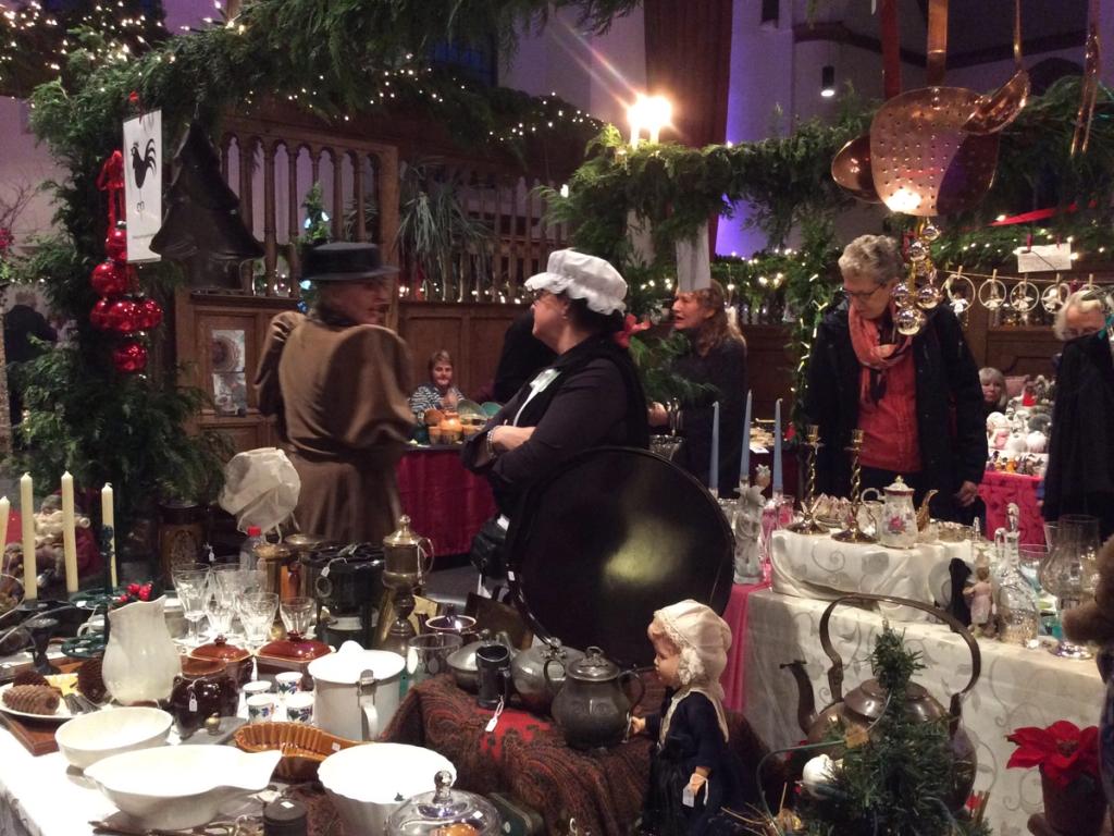 Dickens-figuren in ouderwetse kleding achter een kraam met servies en theepotten