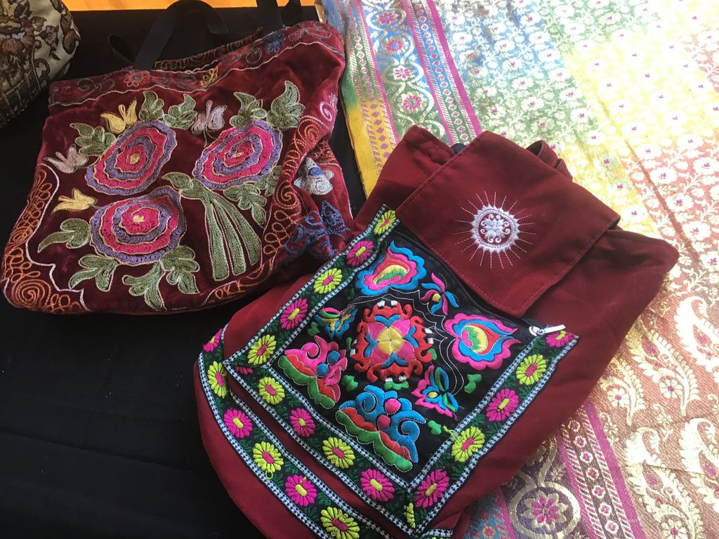 Two embroidered bags in burgundy velvet with colourful flowers, on a colourful cloth