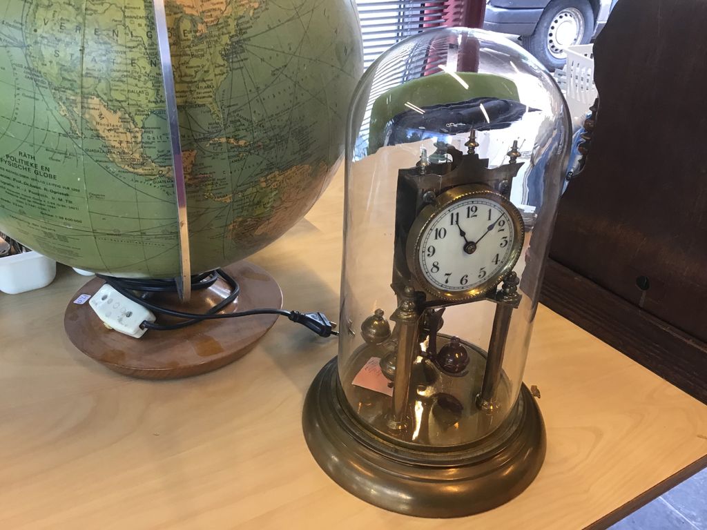 Copper clock under a glass dome next to an old globe