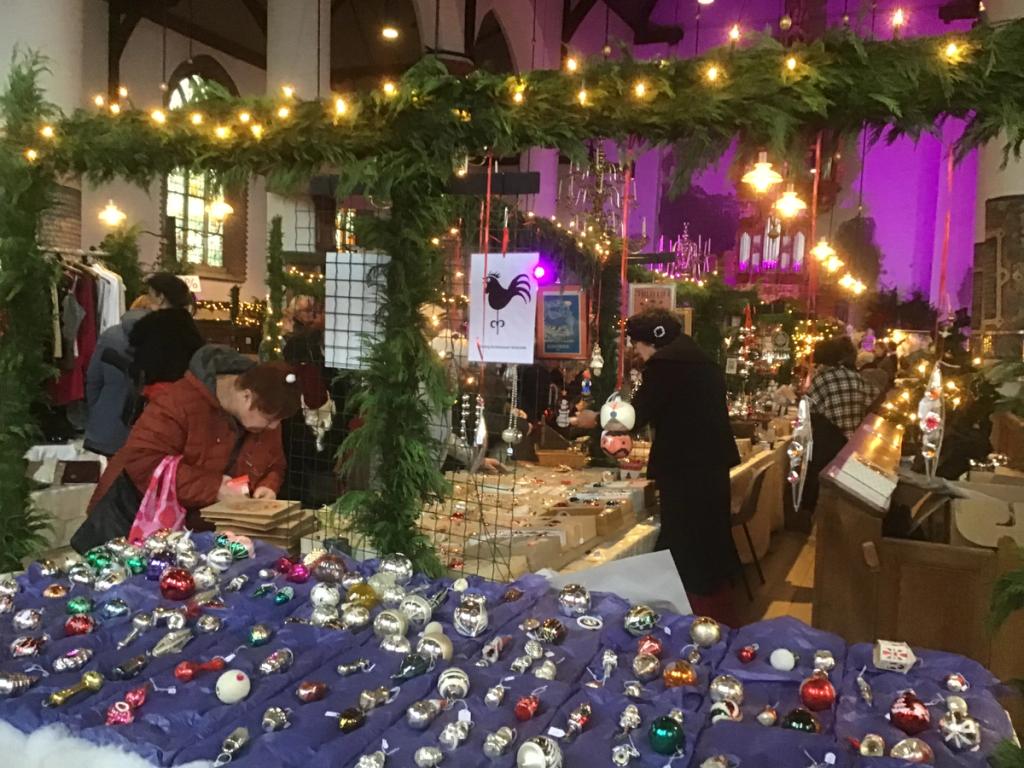 Stall full of glass Christmas baubles on blue cloths under an arch of pine branches with lights in the church