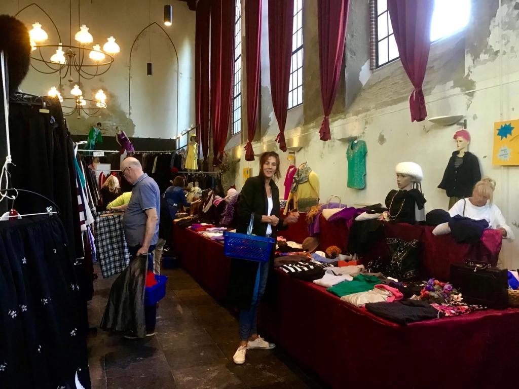 Bezoekers bij een rode tafel met kleding, onder kroonluchters