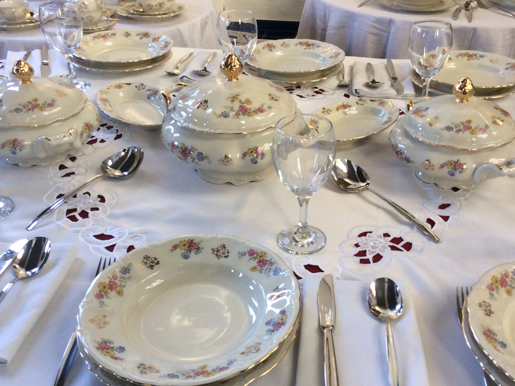 Laid table with white tableware with a flower pattern, soup tureens, wine glasses and cutlery