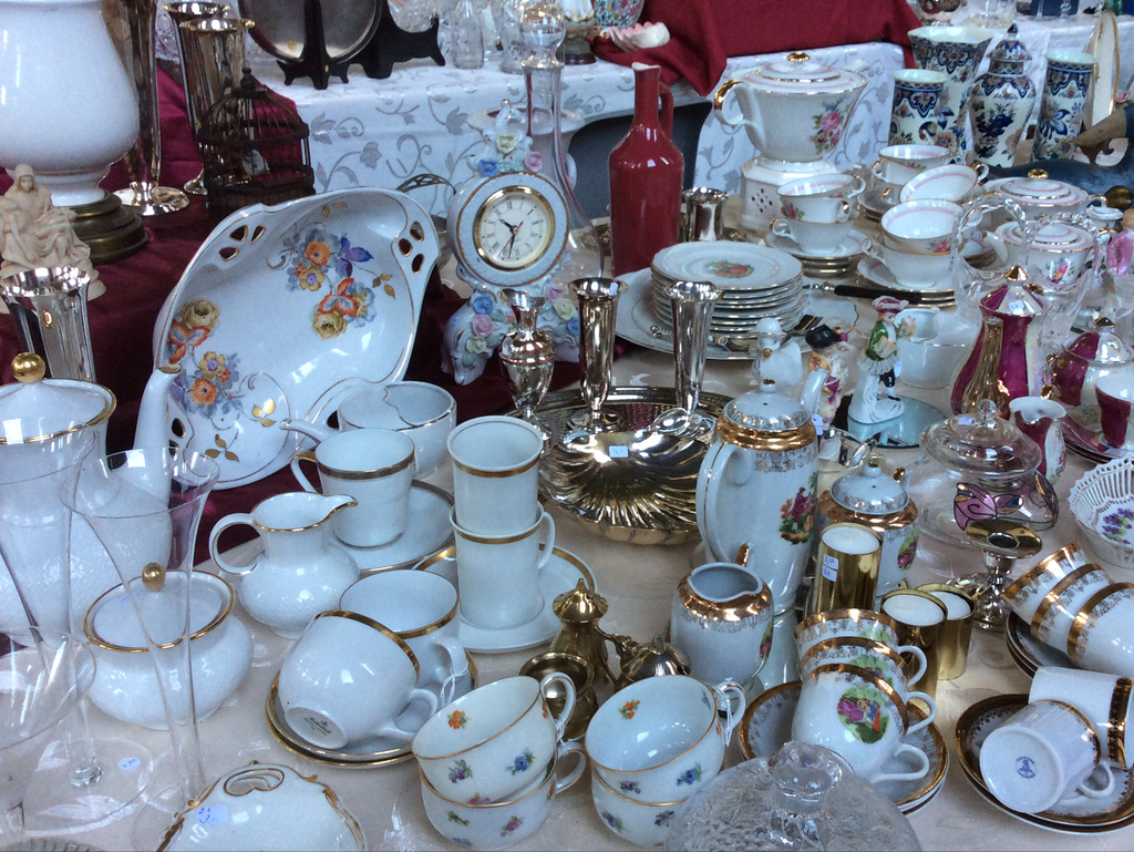 White porcelain with gold edges: cups, jugs, clock and flower bowl on a table with a red cloth