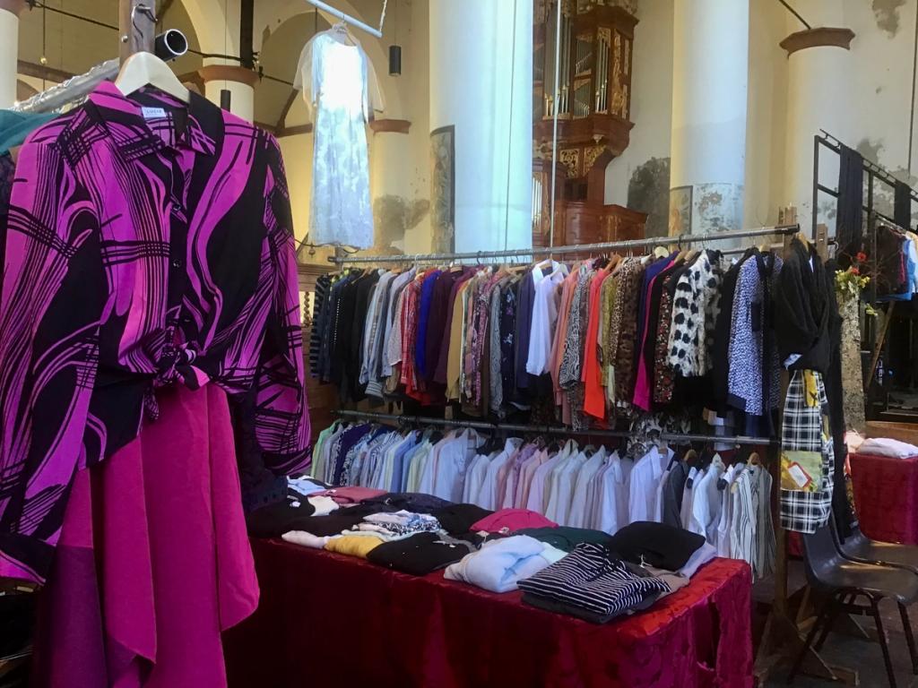 Roze en paarse blouses aan rekken, naast een tafel met truien
