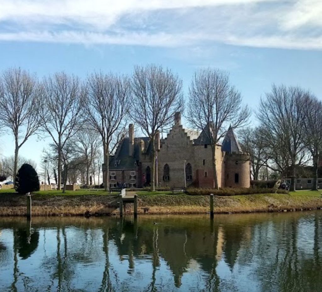 Kasteel Radboud met trapgevel en ronde toren, gezien over het water tussen kale bomen