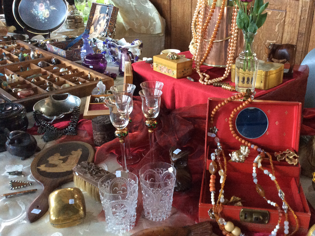 Bead necklaces in a red jewellery box, small crystal glasses, a mirror and boxes on a red cloth