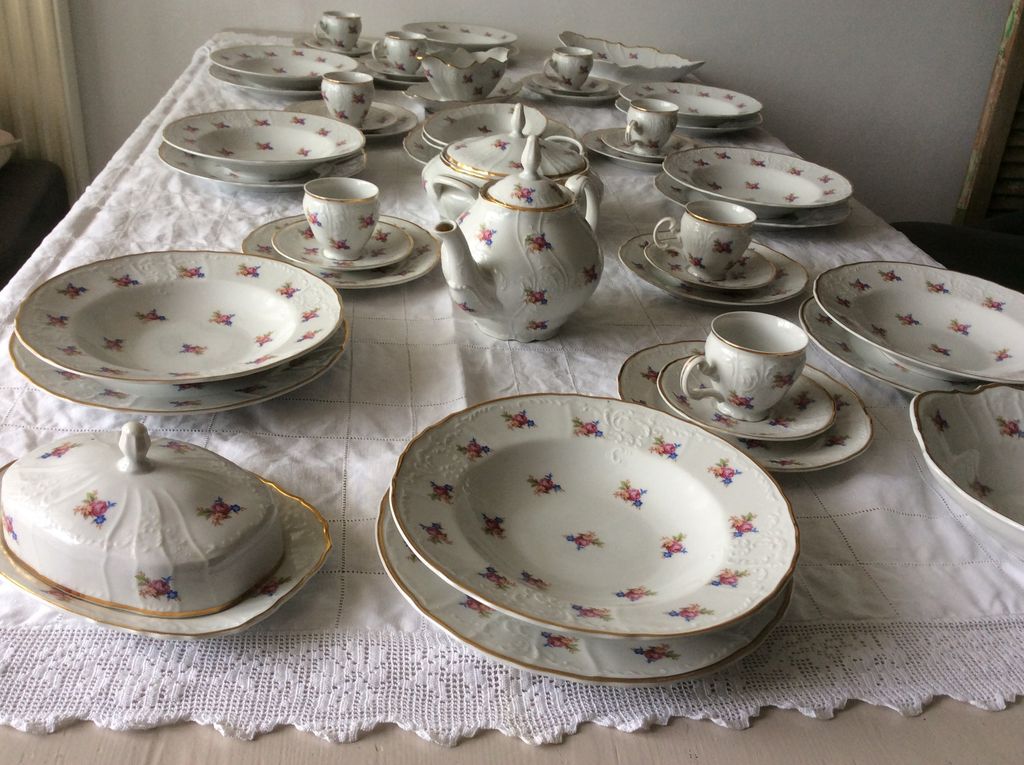 White crockery with small roses and gold edges: plates, cups, teapot and butter dish on a lace cloth