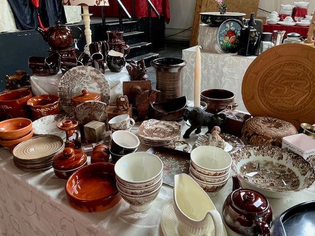 Bruin en oranje aardewerk, borden, kommen en een houten bord op tafels met wit kleed in de kerk
