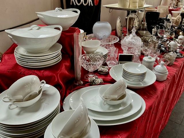 Wit servies met terrines, kopjes, borden en kristal op een tafel met rood kleed