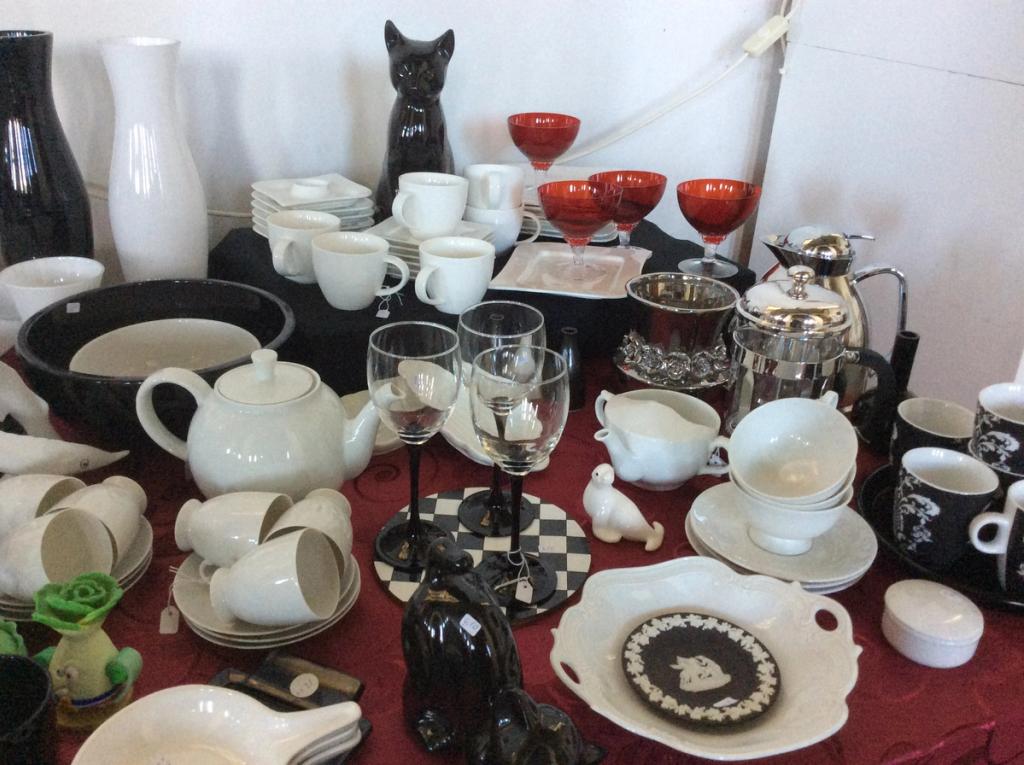White and black tableware with cups, a teapot, red wine glasses, a black cat and a coffee pot on a red cloth