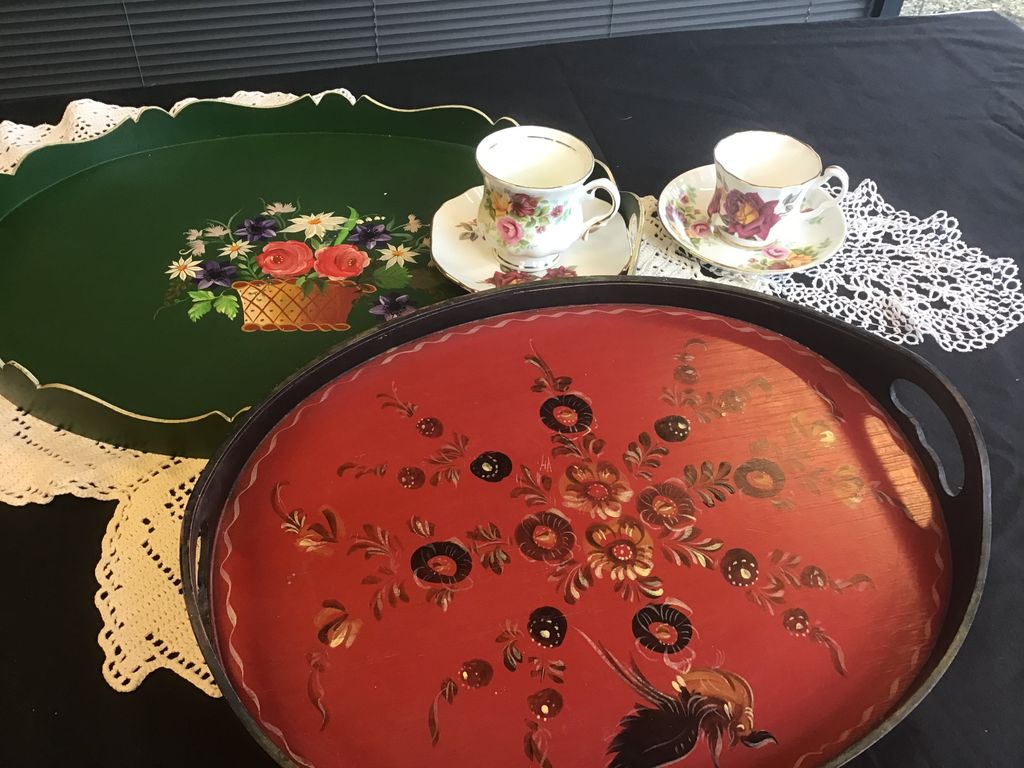 Green tray with a flower basket, red wooden tray with flowers and two cups with roses on lace doilies