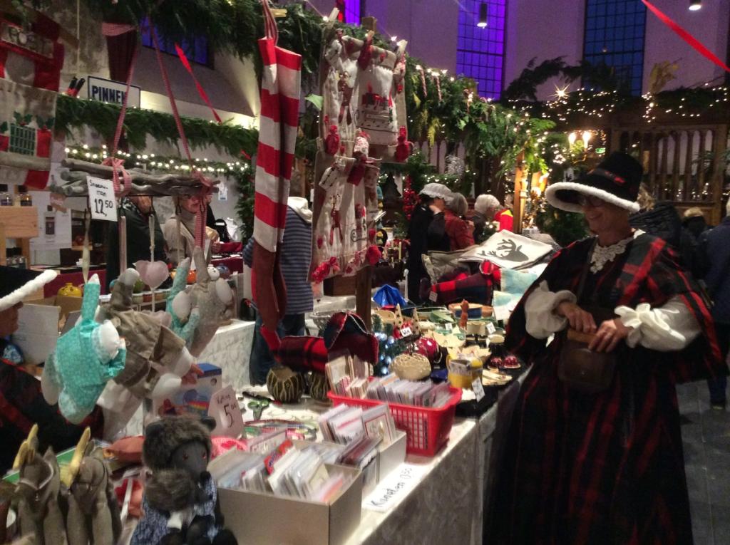 Kraam met knuffels, kerstsokken en kaarten, ervoor een vrouw in Dickens-kleding