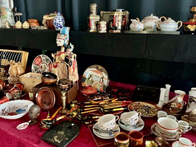 Tafel met Aziatisch servies, blikken, lepels, een houten poppetje en kopjes op een rood kleed
