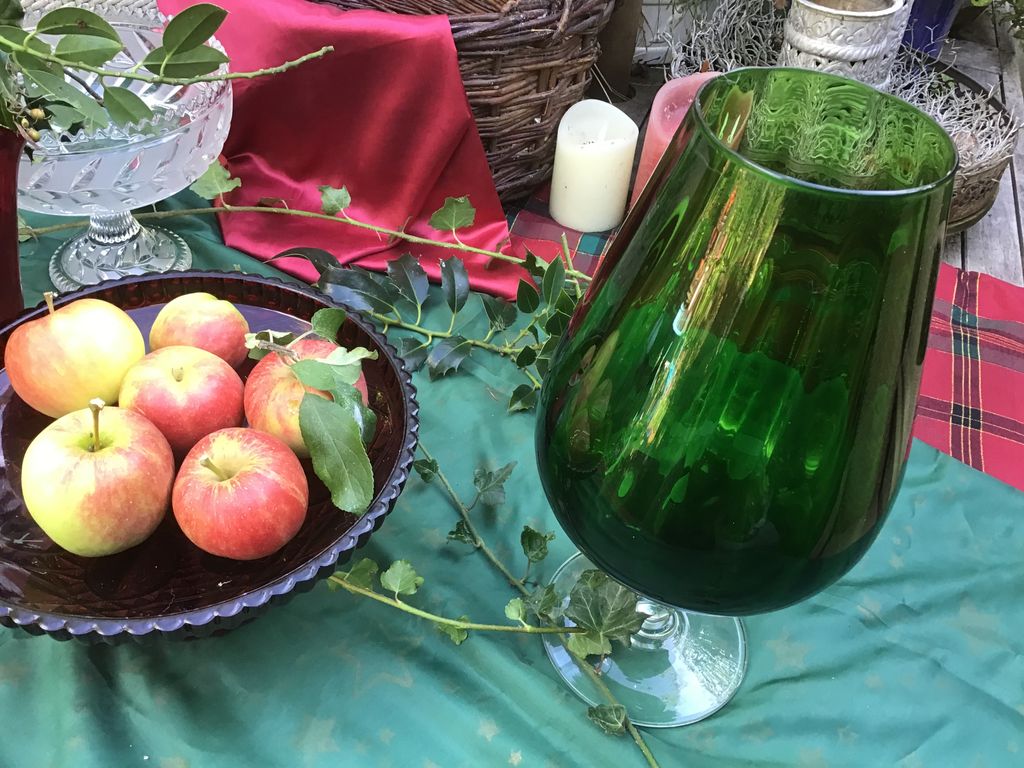 Large green glass vase next to a bowl of apples on a green cloth
