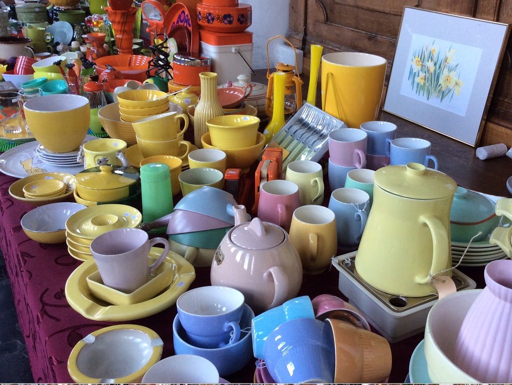 Colourful crockery in yellow, pink, blue and green: cups, bowls, teapot and jug on a table with a burgundy cloth
