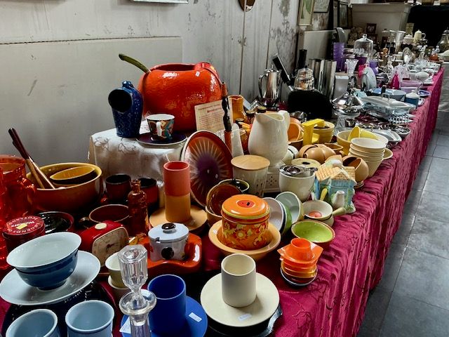 Kleurig retro-servies in oranje, geel en blauw, kommen en kopjes op een lange tafel met rood kleed