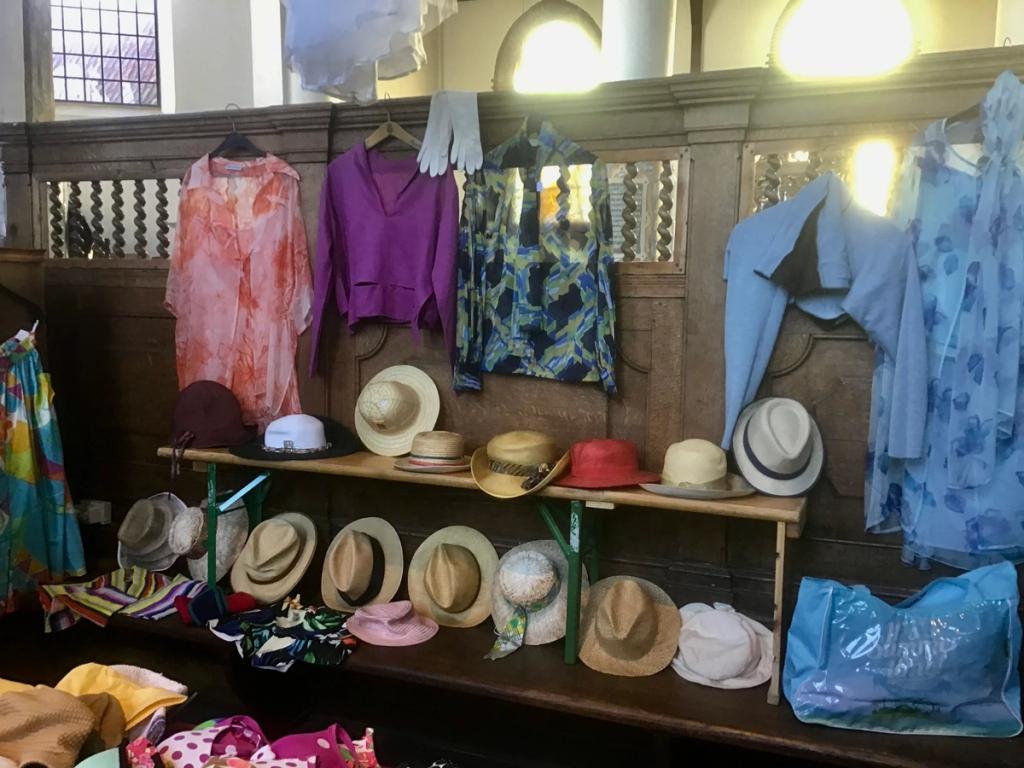 Zomerkleding en hoeden aan een houten wand, met een blauwe tas