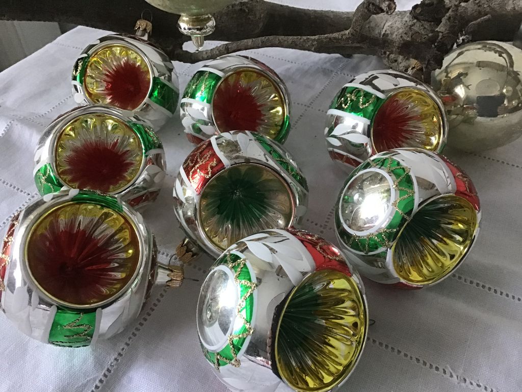 Acht zilveren kerstballen met groene en rode inhammen op een wit kleed
