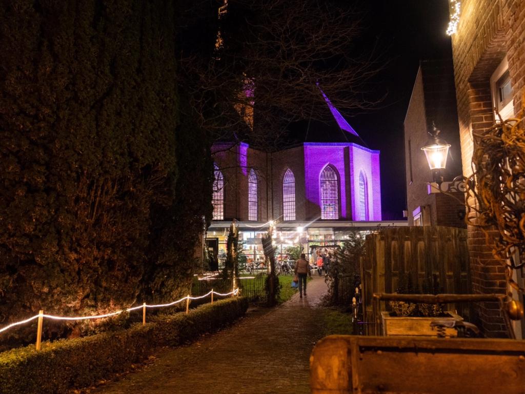 Verlichte tuin met kerkpad en de paars verlichte Bonifaciuskerk in de avond