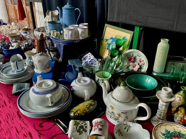 Kleurrijk servies, blauwe emaillen kan, kopjes, theepot en groene glazen op een rood kleed