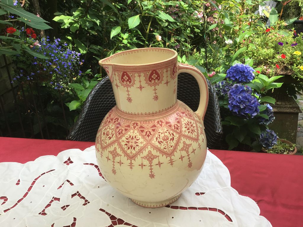 Crèmekleurige kan met rood patroon op een kanten kleed in de tuin