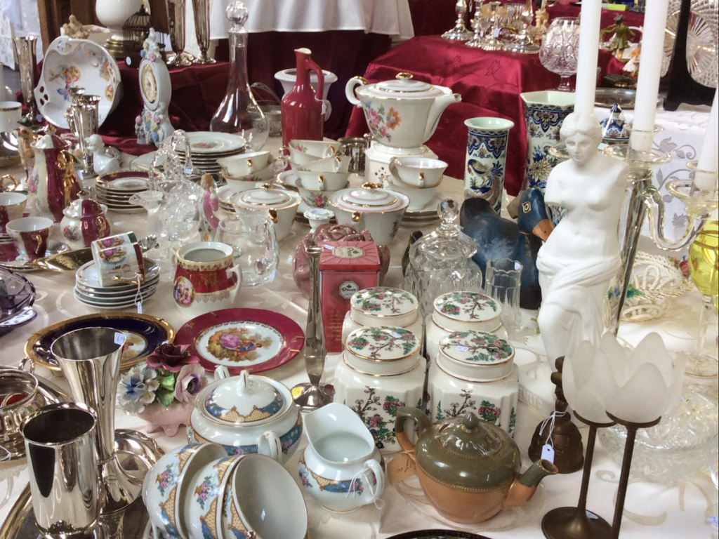 Table full of porcelain, teapots, a white statue of Venus and small silver vases