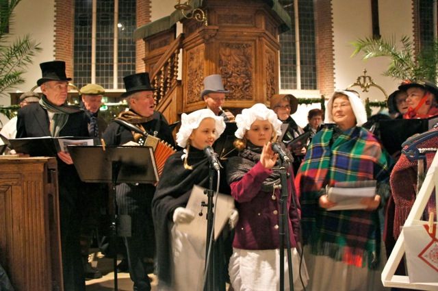 Choir in Dickens clothing singing with music stands in front of the pulpit