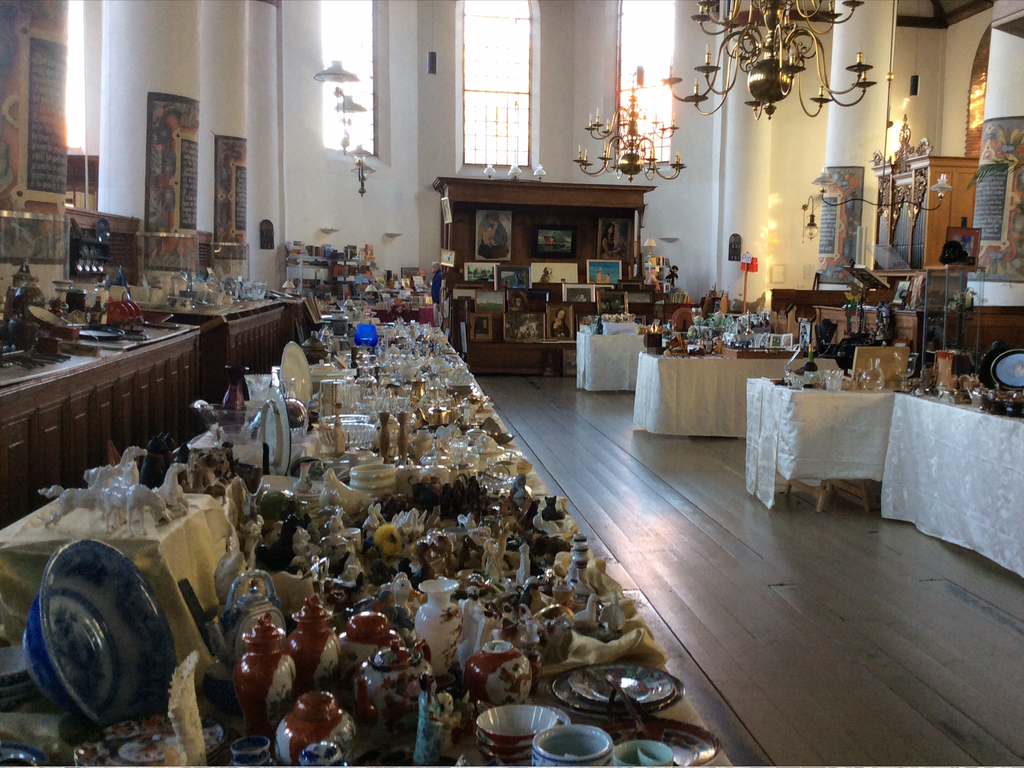 Long market stalls full of porcelain, figurines and glassware in the church with chandeliers and tall windows