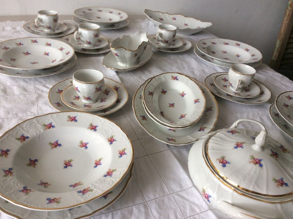White crockery with small roses and a gold edge on a lace cloth: plates, cups, gravy boat and soup tureen