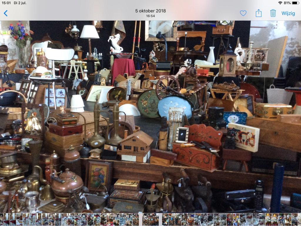 Crowded stall with copper jugs, wooden boxes, a lantern, small paintings and other antiques